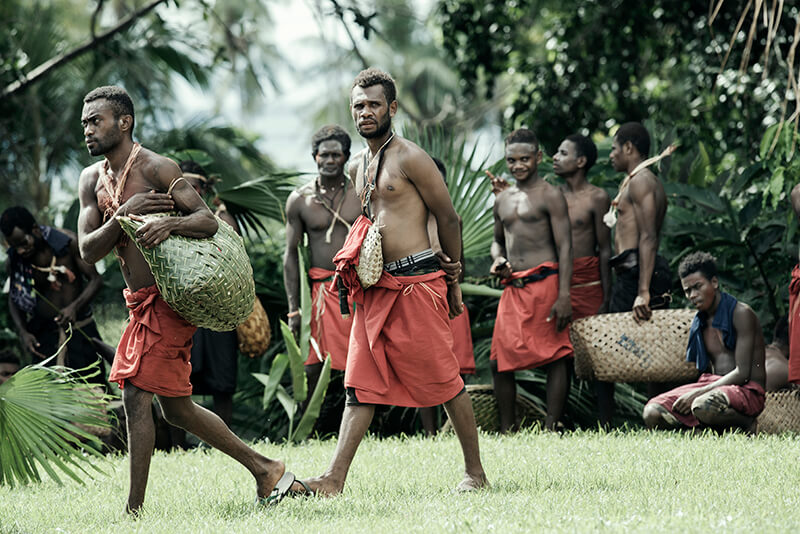 Several tribesmen walk across the scene in their tradition red garments.