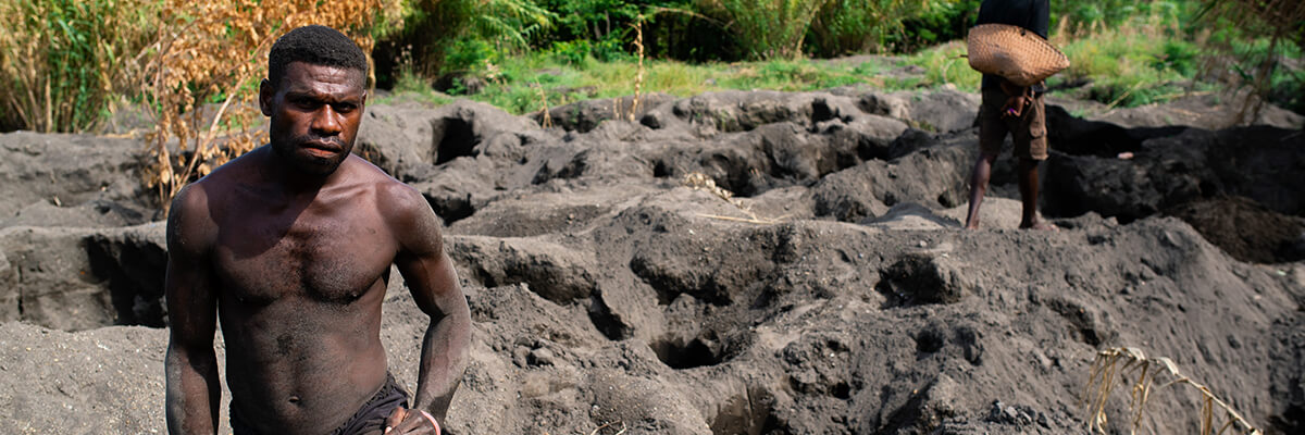 A tribesman crouches on the volcanic dirt.